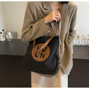 Close-up of black canvas tote bag with adjustable leather strap and HU LN logo patch