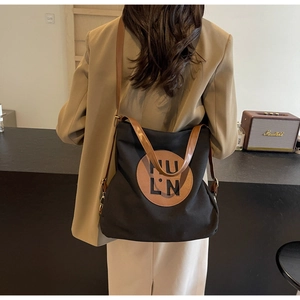 Detail view of black canvas tote bag with brown leather straps worn by a model