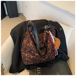 Detail of leopard print tote bag with plush bear charm and leather strap on a sofa