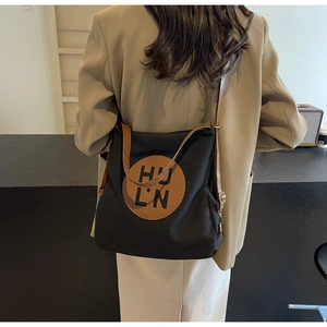Detail of black canvas tote bag with brown leather strap and logo patch on model
