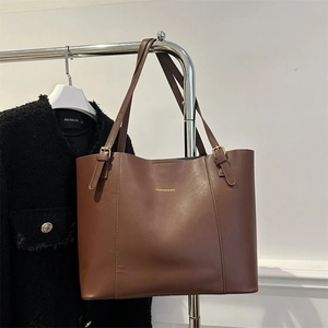 Detail of deep brown tote bag featuring adjustable leather straps and gold metal buckles