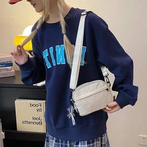 Cream nylon crossbody bag with wide shoulder strap and bear charm on model