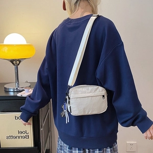 Lightweight cream nylon crossbody bag with dual zippers and checkered bear pendant