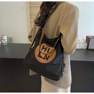 Detail of minimalist black canvas tote bag with brown leather handles and circular logo
