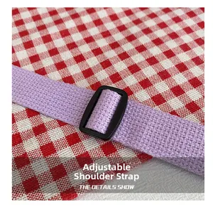 Detail of purple woven adjustable shoulder strap with black plastic buckle and plaid background