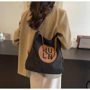 Detail of black canvas tote bag with brown leather handles worn by a model in a beige suit