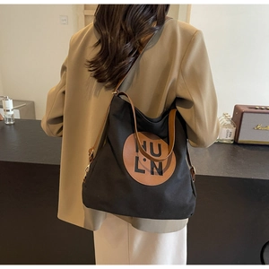 Detail of black canvas tote bag with brown leather straps and HU LN logo patch