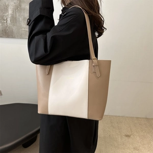 Detail of a large two-tone cream tote bag featuring leather texture and metal strap buckles