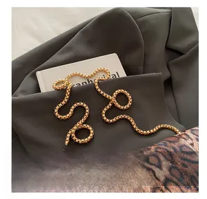 Détail d'une bandoulière chaîne dorée sur sac léopard posé sur une veste grise chic