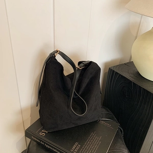 Minimalist black suede tote bag with adjustable leather strap on a stylish wooden side table
