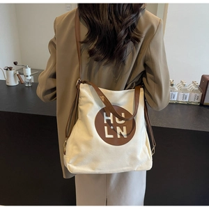 Detail of minimalist canvas tote bag with brown leather patch and HU LN lettering logo