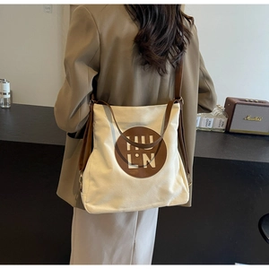 Detail of canvas tote bag featuring a leather logo patch and brown shoulder strap