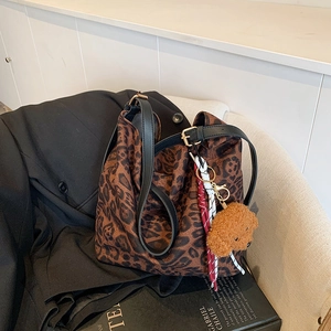 Leopard print tote bag with black leather straps and a plush bear pendant on a suit