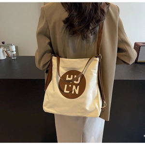 Detailed view of canvas tote bag showing brown leather handles and circular logo patch