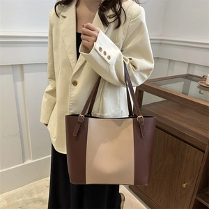 Detail shot of a brown and beige patchwork tote bag worn with a stylish blazer