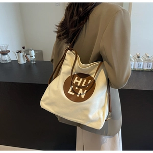 Chic cream canvas tote bag with brown leather handles worn in a stylish cafe setting