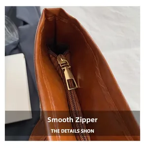 Detail view of the smooth golden metal zipper and high-quality stitching on brown leather bag