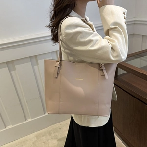 Detail view of a beige faux leather tote bag showing stitching and logo print on the model