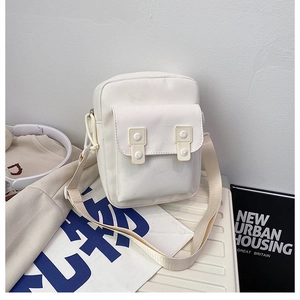 Macro detail of a white canvas mini crossbody phone bag on a suitcase in a travel scene
