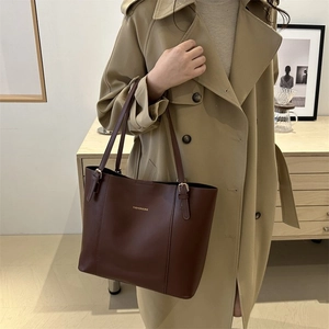 Detail of dark brown leather tote bag with gold lettering styled on a beige trench coat