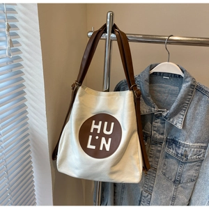 Detailed close-up of a canvas tote bag with brown leather logo patch and shoulder strap