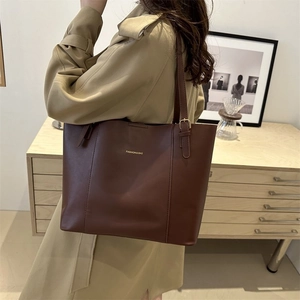 Detail of deep brown leather tote bag with vertical stitching and gold metal buckles