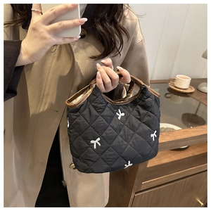 Detail of a black quilted handbag with white bow embroidery and brown leather trim