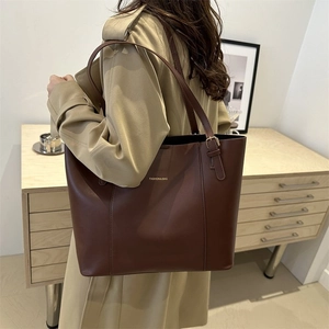 Detail of a large dark brown matte leather tote bag worn with a khaki trench coat