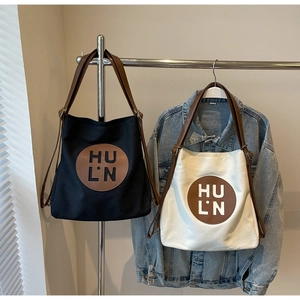 Close-up of canvas tote bag with round leather logo patch and long brown shoulder straps