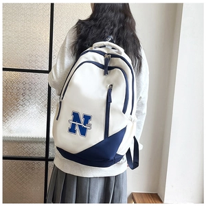 Detailed back view of a white and blue stylish backpack worn by a person in a minimalist room