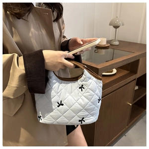Detail of quilted white handbag with black bow embroidery and brown leather handles