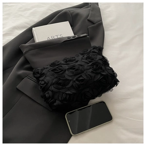 Close-up of black 3D lace flower clutch bag on a bed next to a black blazer