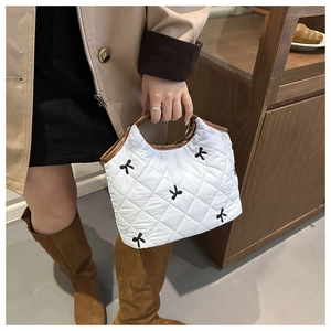Close-up of white quilted handbag with black bow embroidery and brown leather handle