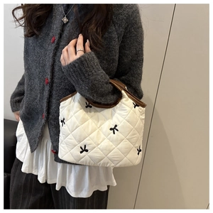 Close-up of quilted white handbag with black bow embroidery and brown trim detail