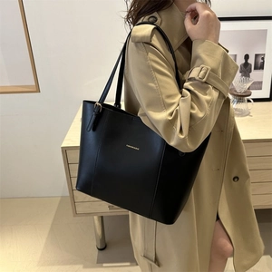 Classic black leather tote bag with gold lettering shown on a trench coat model