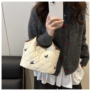Mirror selfie showing the ivory quilted handbag with black bow embroidery and leather handles