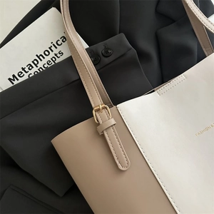 Detail of khaki and beige leather tote bag with gold buckle on a black blazer