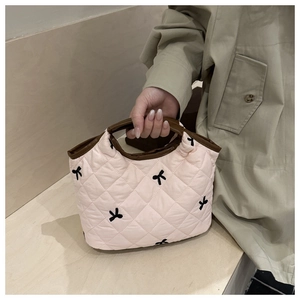 Detail of light pink quilted handbag featuring black bow patterns and leather handles
