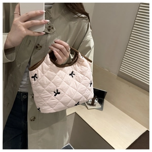 Close-up of pink quilted handbag with black bow embroidery and dark brown leather handle