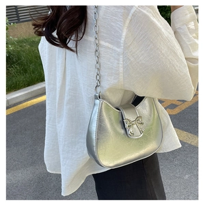 Close-up of silver cracked leather shoulder bag with a gold metal bow buckle and chain