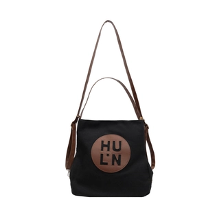 Black canvas tote bag with brown handles and central letter logo in a minimalist design