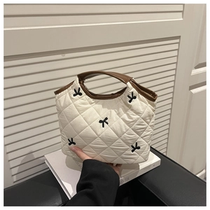 Detail of white quilted handbag with black embroidered bow and brown handles