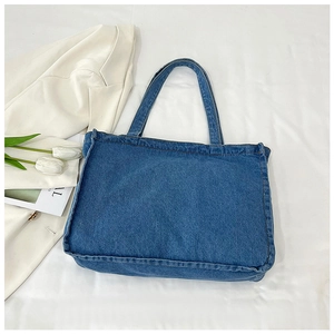 Detail of a large dark blue denim tote bag with dual straps on white bedding