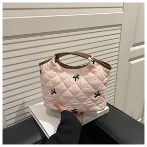 Detail shot of a pink quilted handbag featuring embroidered black bows and brown handles