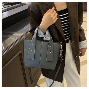 Detail view of grey-blue litchi grain leather tote bag with gold studs and shoulder strap