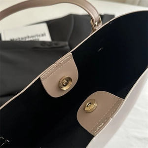 Detail view of large beige leather tote bag featuring double magnetic gold buckle closures
