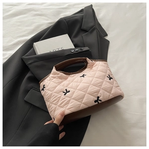 Detailed shot of pink quilted fabric handbag with small black bow embroidery and brown trim