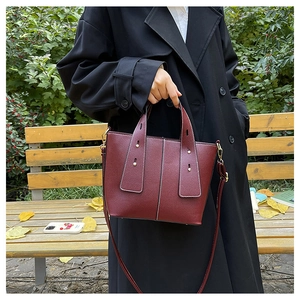 Detail of burgundy leather bucket bag with litchi texture held by model in autumn park