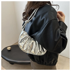 Détail du sac à bandoulière argenté plissé avec nœud de sangle porté par un modèle