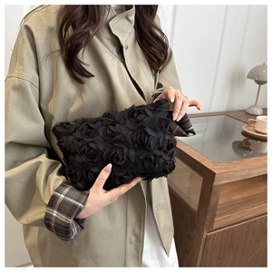 Detail of 3D rose flower texture on a black evening clutch bag held by a model
